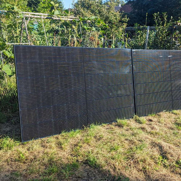 Zwei senkrecht am Gartenzaun montierte Solarmodule vor einem Gemüsegarten