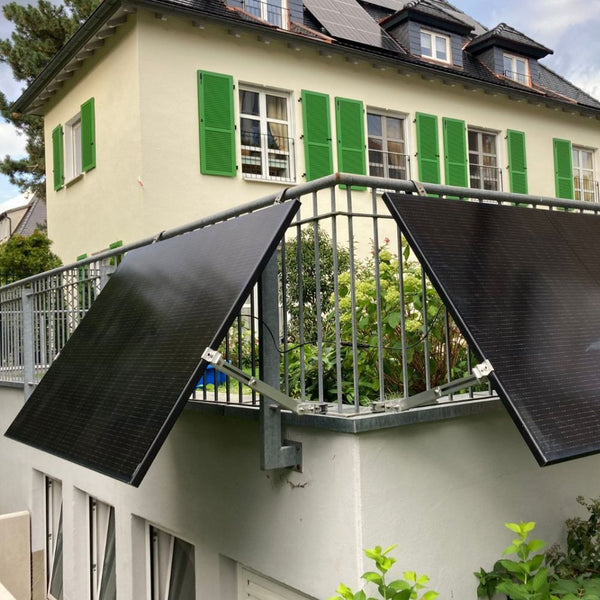 Zwei angewinkelt am Terrassengeländer montierte Solarmodule vor einem Haus mit grünen Fensterläden